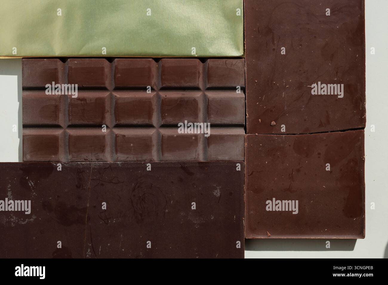 Sfondo di barrette di cioccolato non confezionate. Cioccolato rotto. Una barra in carta laminata gialla. Diverse tonalità di marrone. Vista dall'alto. Foto Stock