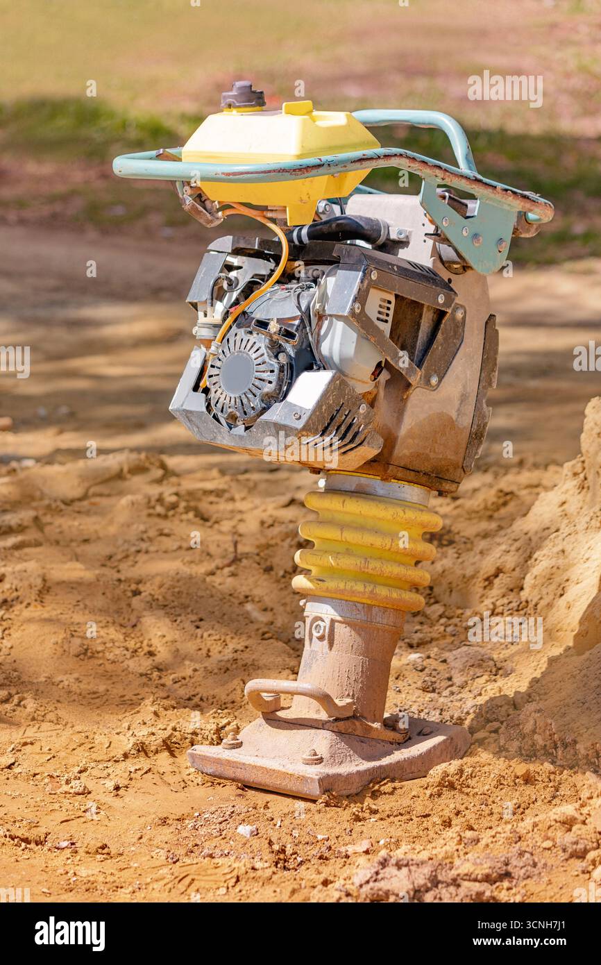 Compattatore a ponte alimentato a benzina che opera diligentemente su terreni sabbiosi in cantiere, garantendo un'efficace compattazione del suolo Foto Stock