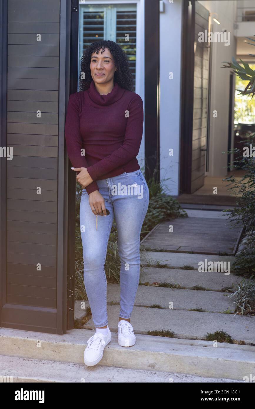 Donna afroamericana appoggiata al pannello accanto alla porta sfinestrata all'ingresso principale, tenendo l'anello portachiavi Foto Stock