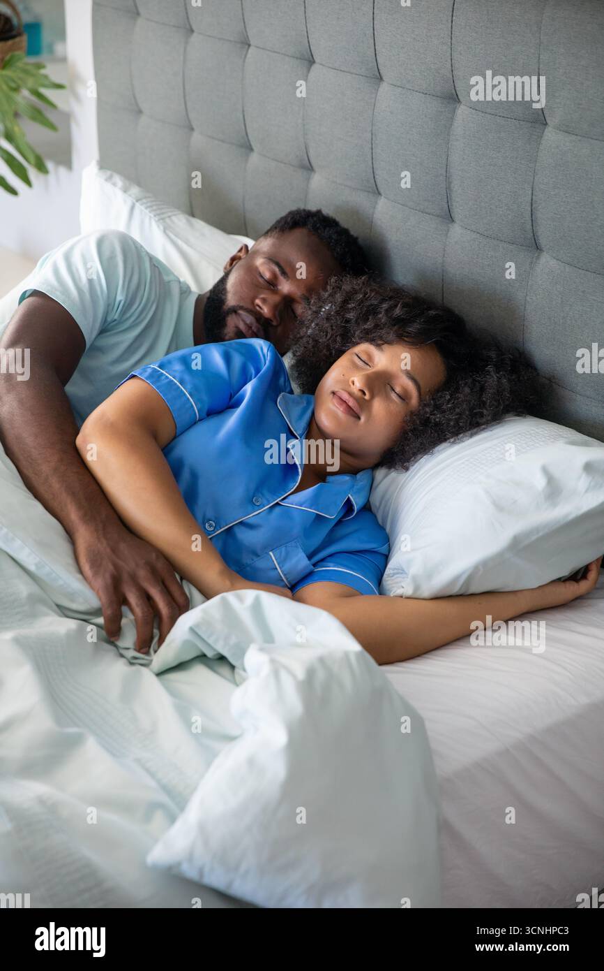 Coppie diverse sdraiate sul letto di casa con maglietta bianca pigiama blu sotto la testata grigia Foto Stock