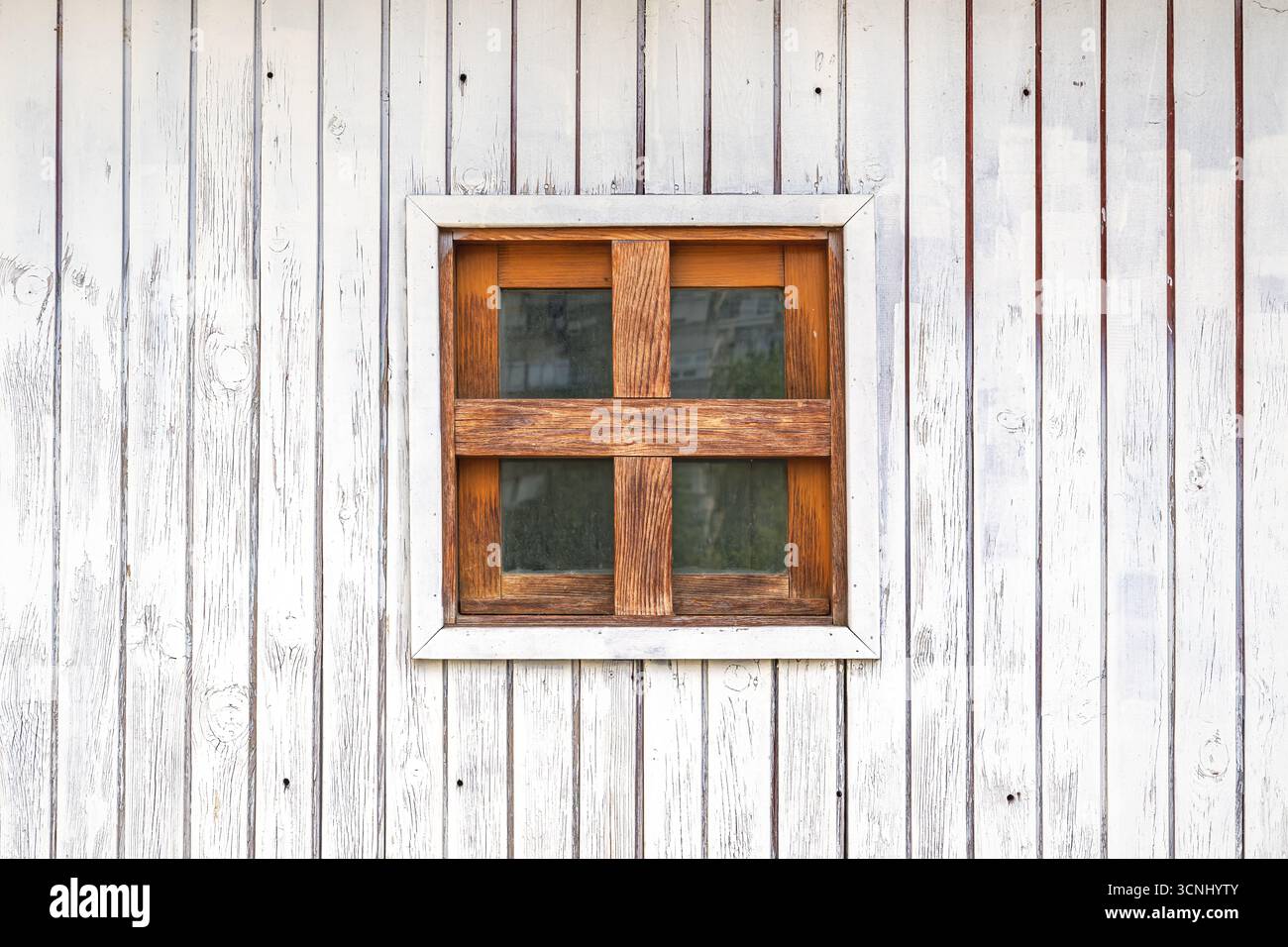 Piccola finestra di legno marrone a forma quadrata sulla parete di legno bianco di un capannone rustico nella campagna slovena, semplice dettaglio architettonico alpino Foto Stock