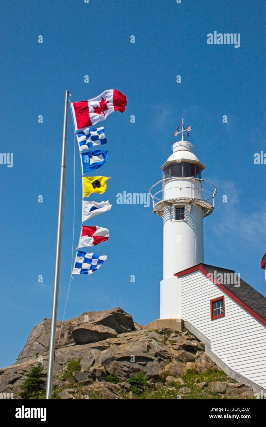 Le bandiere di segnalazione marine sventolano nella brezza accanto al faro di Lobster Cove a Rocky Harbor, Terranova. Il cielo luminoso rende ancora più sereno Foto Stock