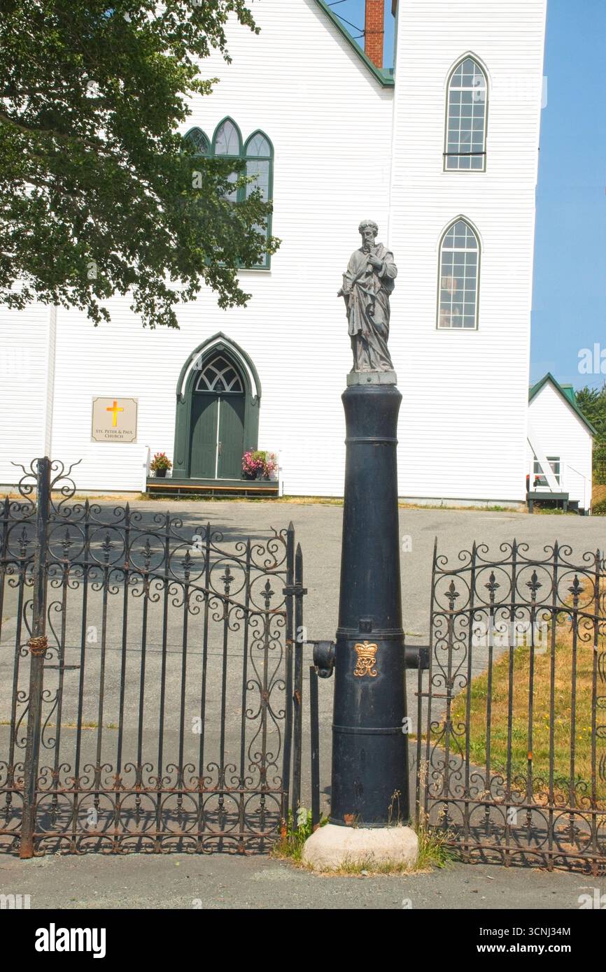 Una statua di un santo sorge su un canone accanto a una porta in ferro battuto che confina con la chiesa di San Pietro e Paolo a Bay Bulls, Terranova Foto Stock