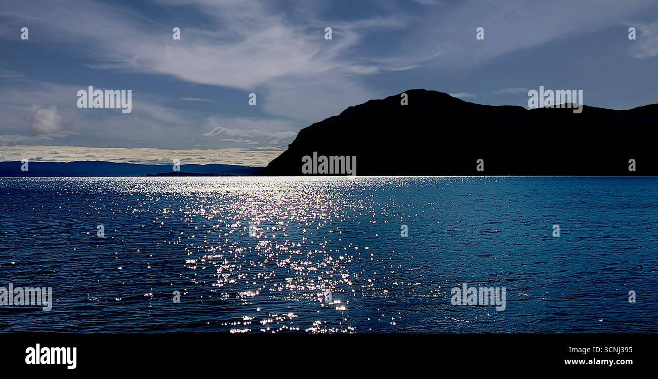 L'acqua cristallina della Baia delle Isole di Terranova risplende sotto la luce del sole con un'impressionante silhouette di montagna in lontananza. Deriva delle nuvole in t Foto Stock