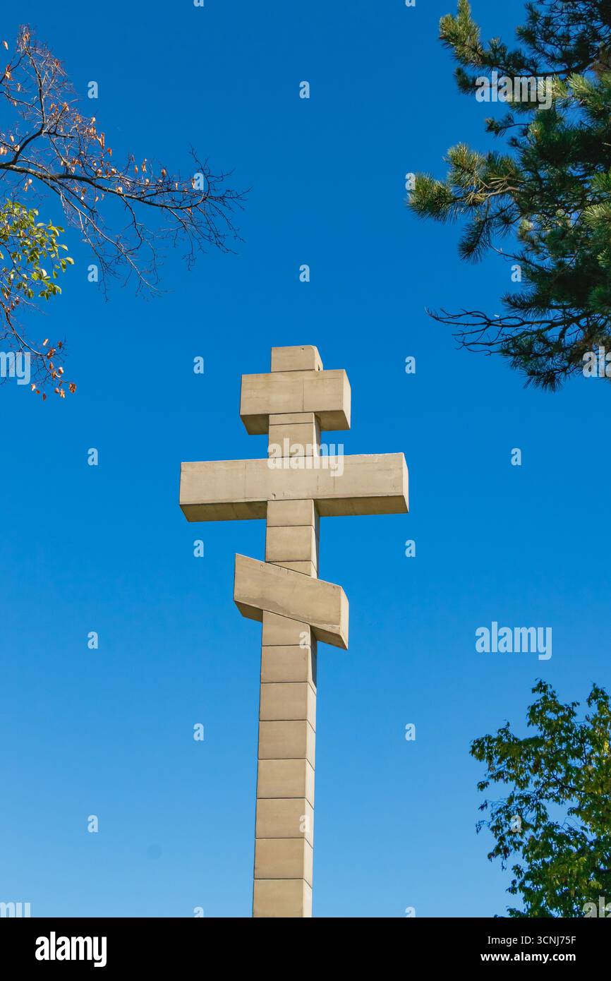 Alta croce in pietra ortodossa con due barre orizzontali in piedi sotto il cielo azzurro, che rappresentano la fede cristiana, la spiritualità, la tradizione e la religione Foto Stock