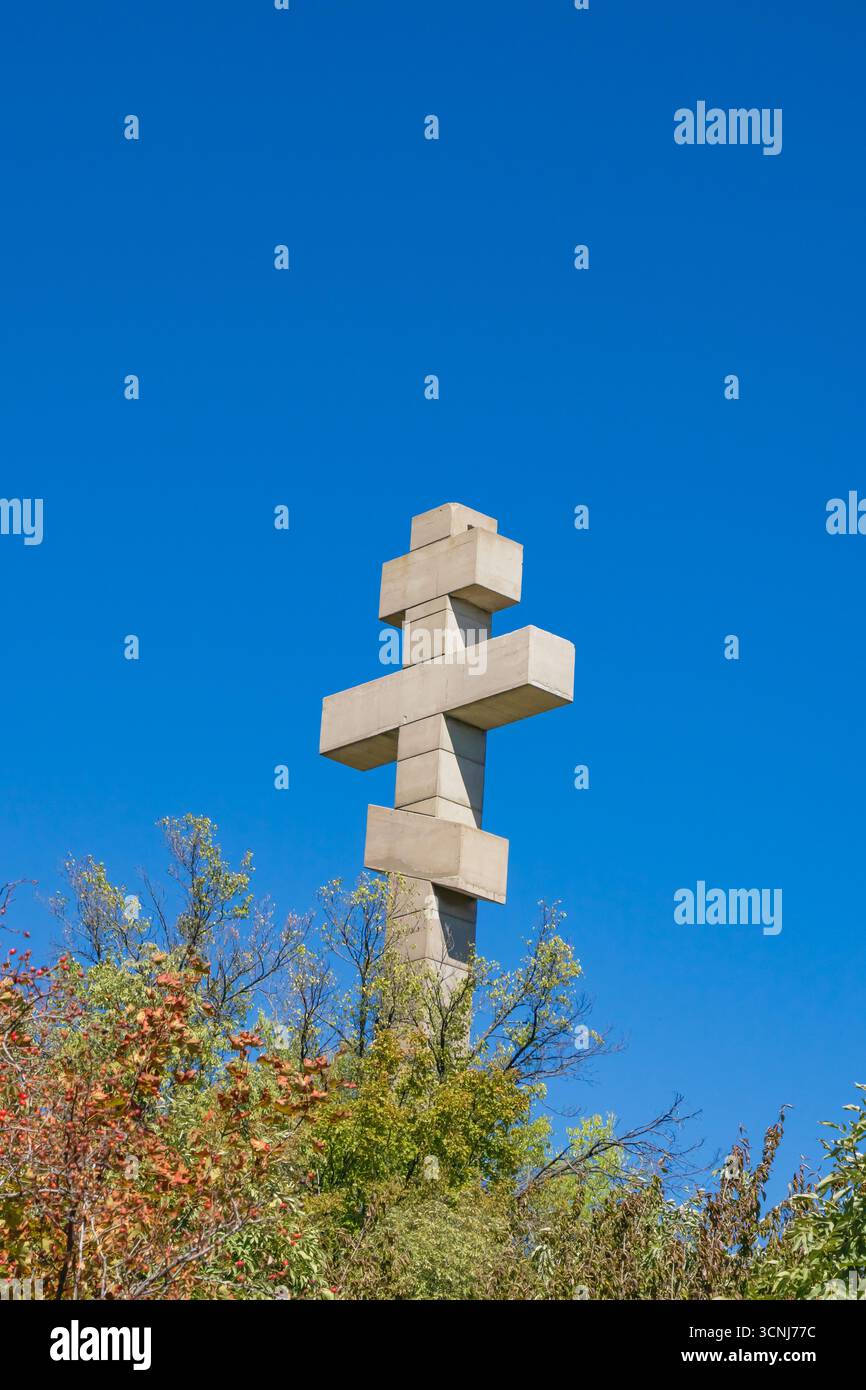 Il grande monumento a croce ortodossa si erge alto sopra colorati alberi autunnali, sagomato contro un cielo blu limpido, a simboleggiare la fede e la spiritualità in un Foto Stock