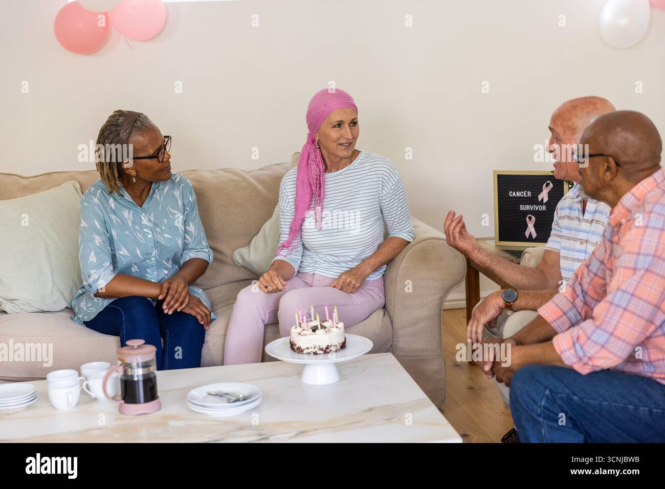 Amici diversi si riuniscono intorno al tavolo a casa con torta, tazze da caffè, segno di sopravvissuto al cancro Foto Stock