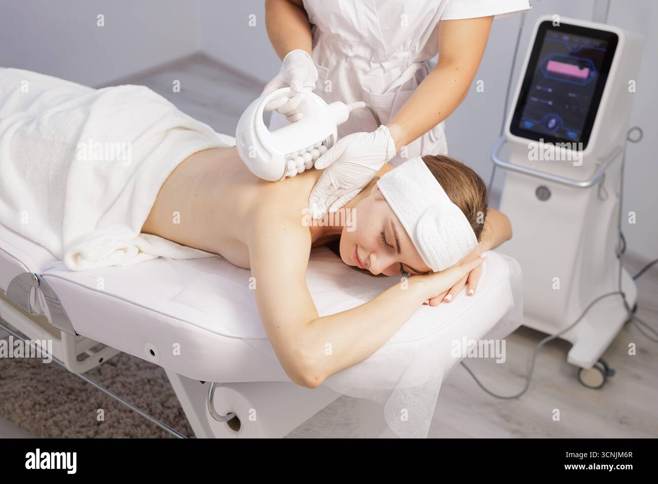 Terapista professionista esegue un massaggio alla schiena anti cellulite utilizzando un dispositivo a rullo in una clinica termale luminosa e pulita per il benessere e il rassodamento della pelle. Foto Stock