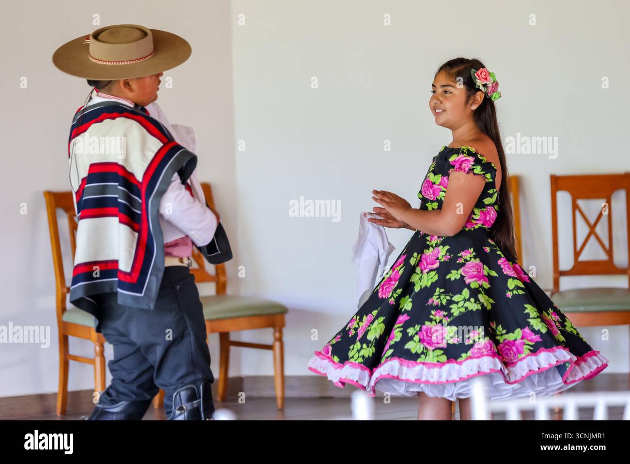 Una giovane coppia esegue la tradizionale danza cueca cilena, vestita con vivaci costumi folcloristici, all'interno di un luogo culturale. Foto Stock