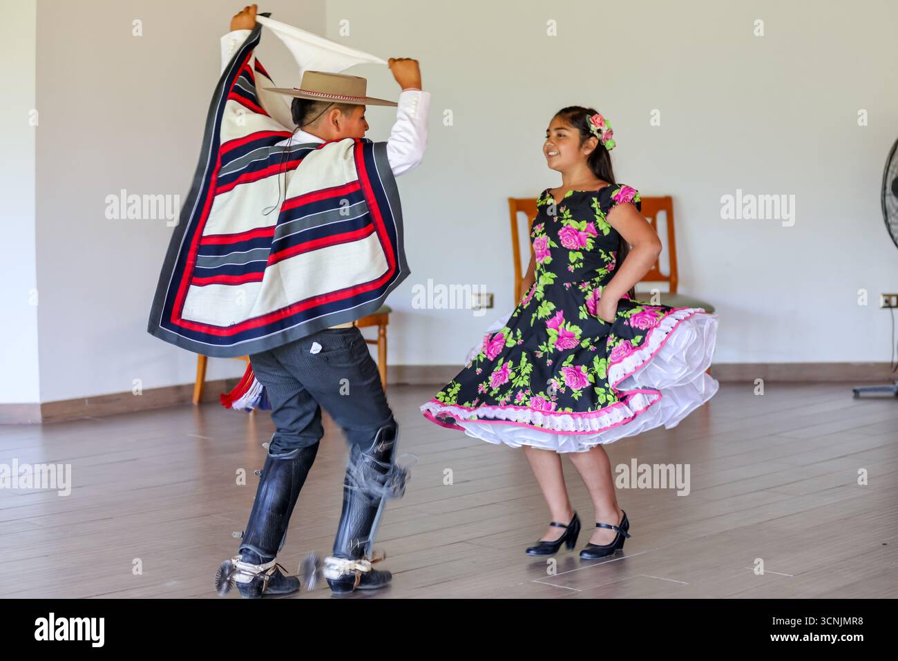 Una giovane coppia esegue la tradizionale danza cueca cilena, vestita con vivaci costumi folcloristici, all'interno di un luogo culturale. Foto Stock
