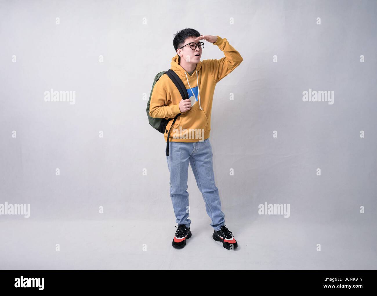 giovane uomo con zaino in felpa gialla in posa salutista in un ritratto in studio Foto Stock