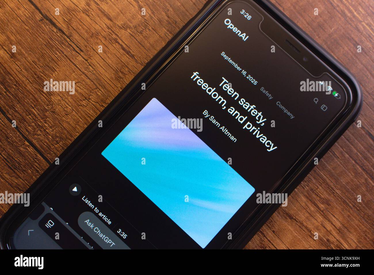 Primo piano dello schermo dello smartphone che mostra un articolo OpenAI sulla sicurezza, la libertà e la privacy degli adolescenti su un tavolo di legno. Foto Stock