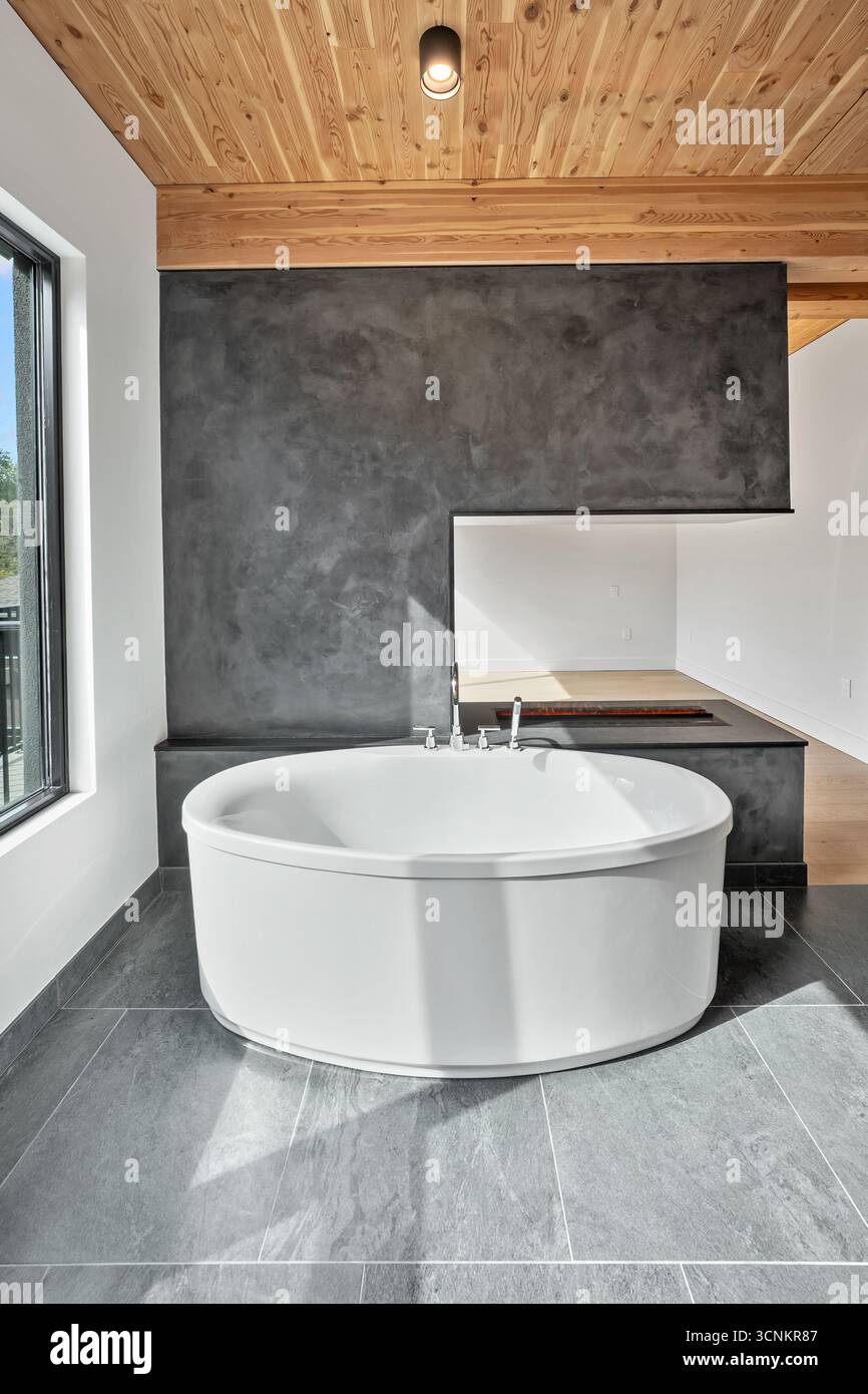 Grande vasca da bagno bianca con pavimento in piastrelle grigie. La camera è ben illuminata e presenta un'estetica moderna e pulita Foto Stock