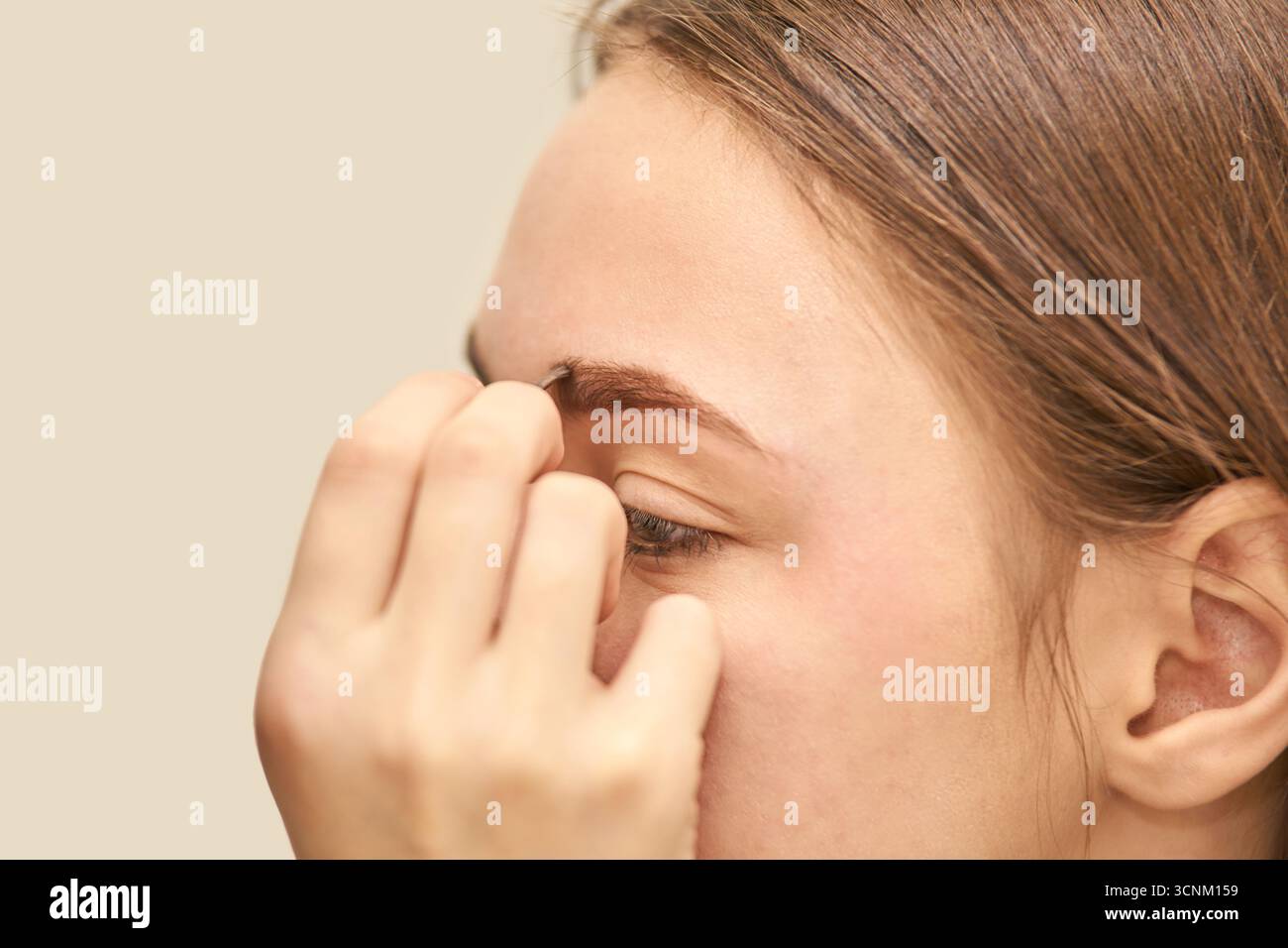 Giovane donna caucasica che abbronza le sopracciglia in primo piano su sfondo beige, con particolare attenzione alla cura della persona e della cura del corpo. Foto Stock