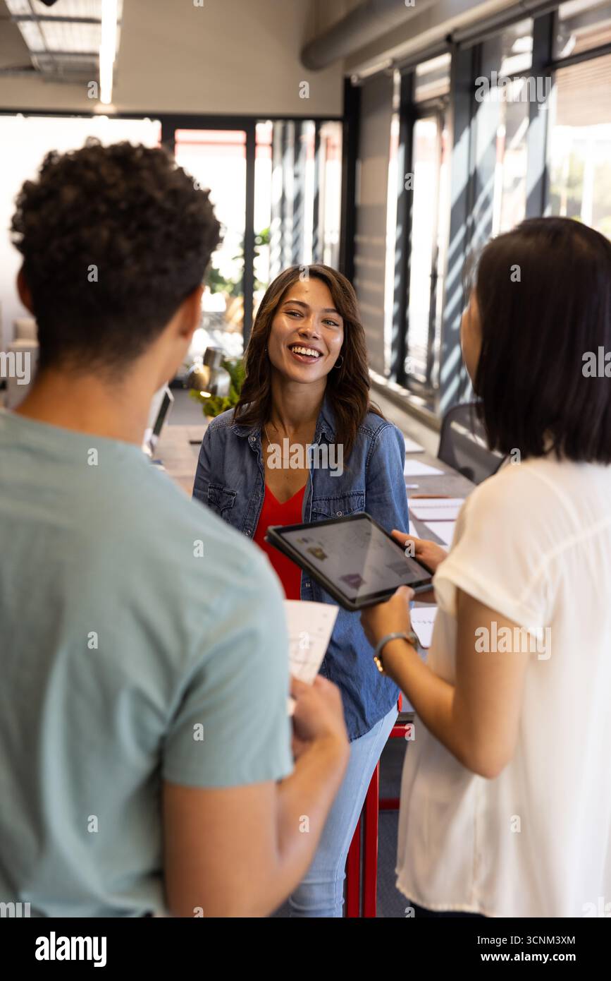 Diversi colleghi che collaborano con documenti stampati e utilizzano un tablet alla scrivania dell'ufficio Foto Stock
