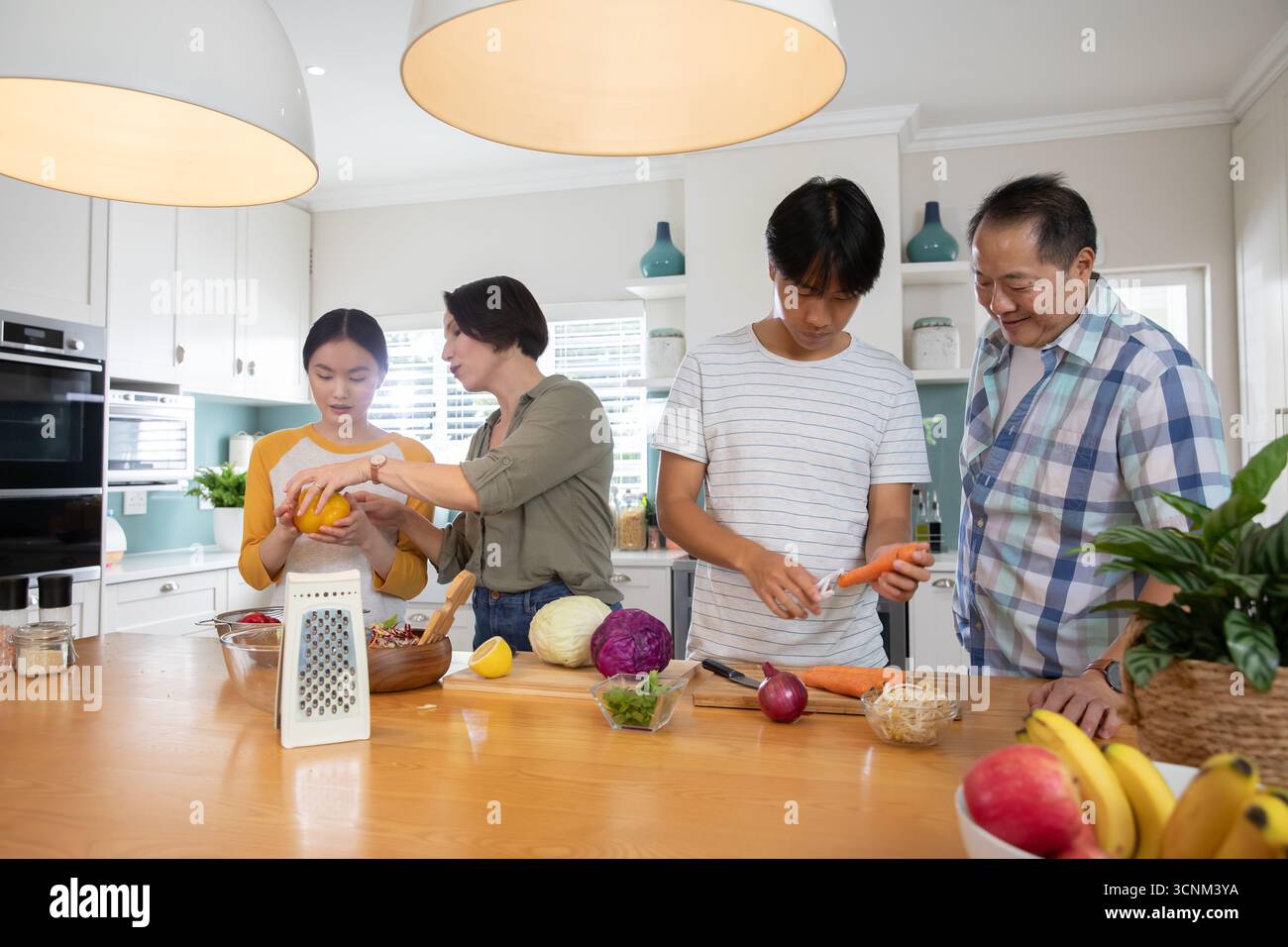 Una famiglia di quattro persone che si trova intorno all'isola di cucina, affettando peperoni e pelando carote Foto Stock
