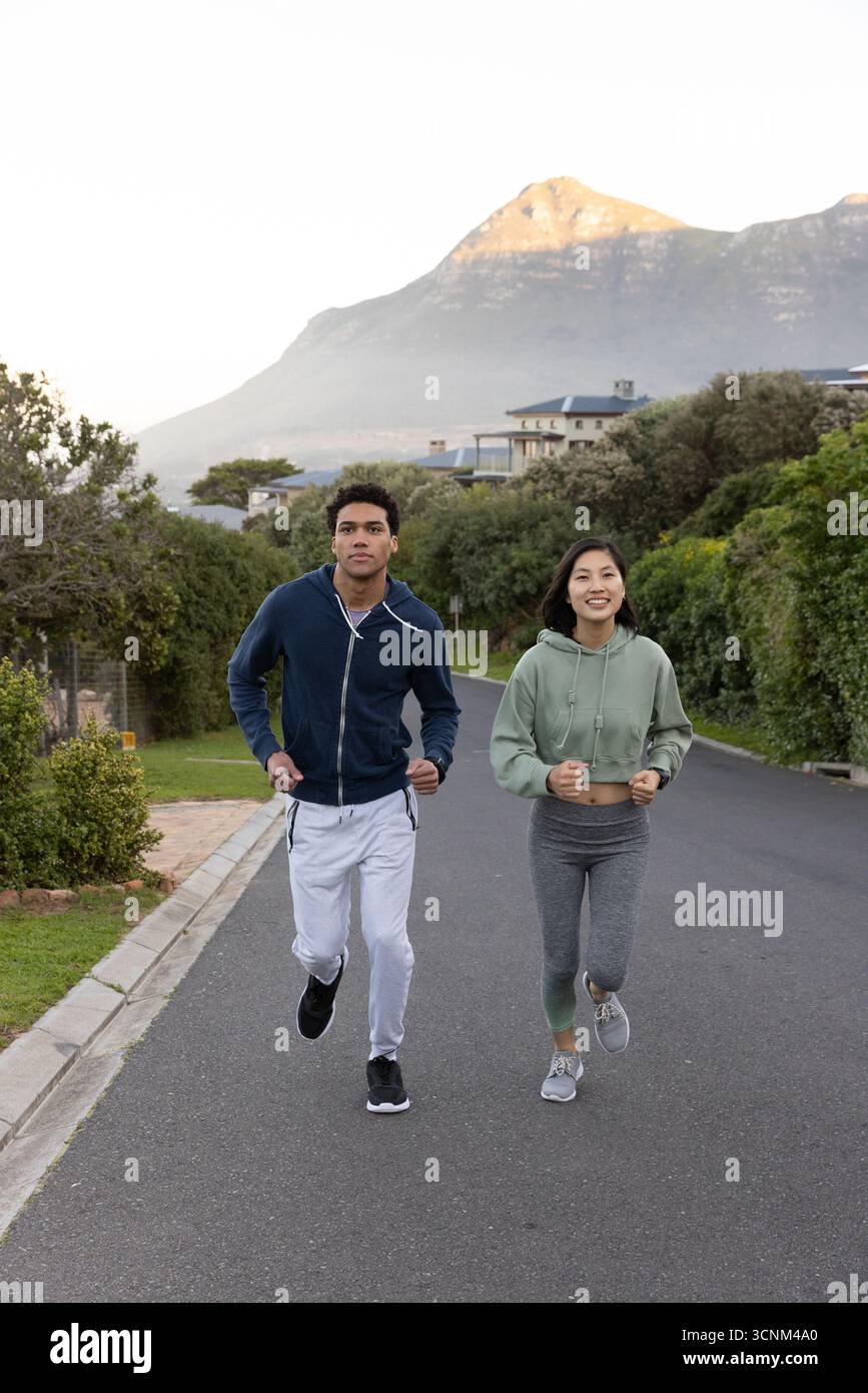 Diverse coppie che fanno jogging insieme per strada alla base della montagna con felpe con cappuccio e scarpe da running Foto Stock