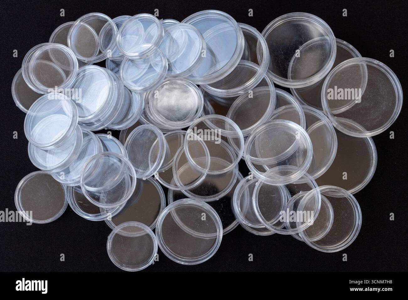 Capsule a bottone in plastica trasparente sparse su sfondo nero Foto Stock