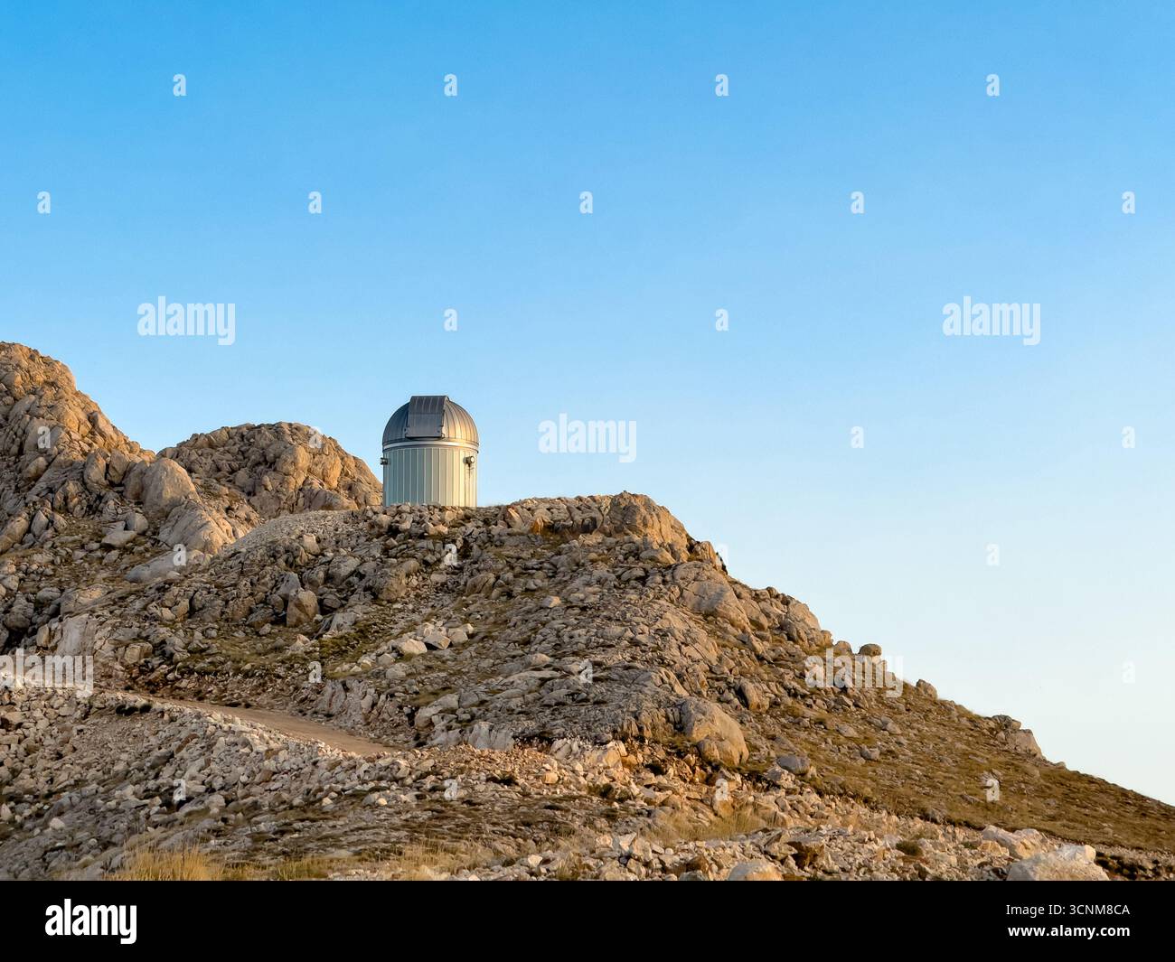 Cupola dell'osservatorio arroccata su una collina rocciosa sotto il cielo azzurro Foto Stock