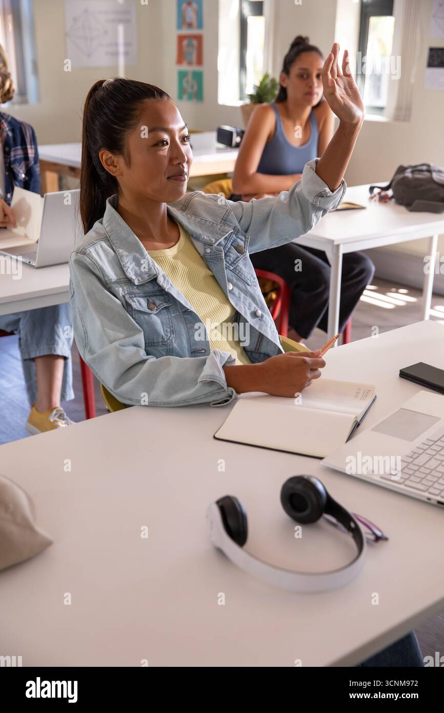 Studentesse che alzano la mano, scrivono su un notebook con una matita e scrivono su un notebook Foto Stock