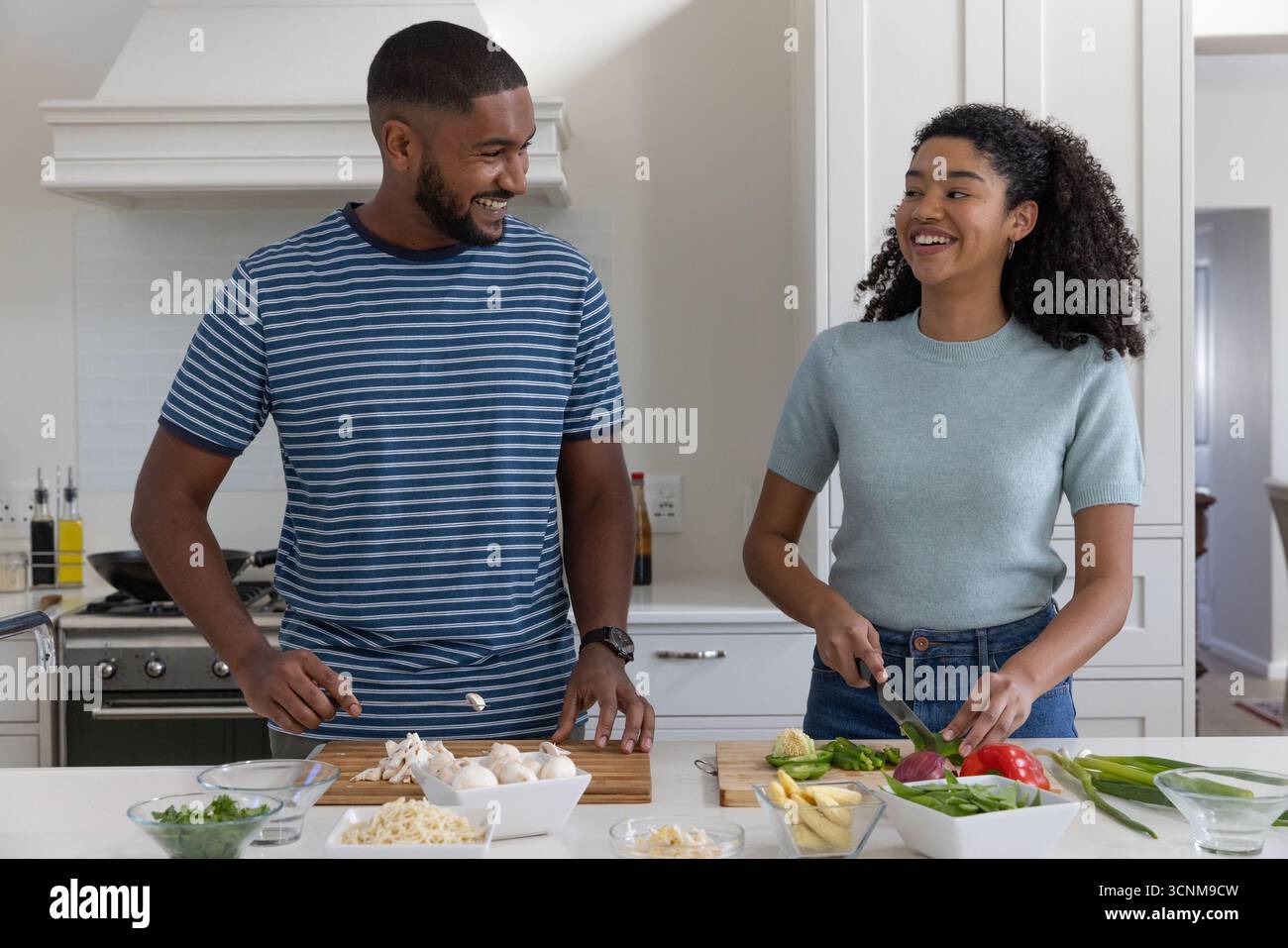 Diverse coppie che affettano asparagi e peperoni sui taglieri dell'isola della cucina Foto Stock