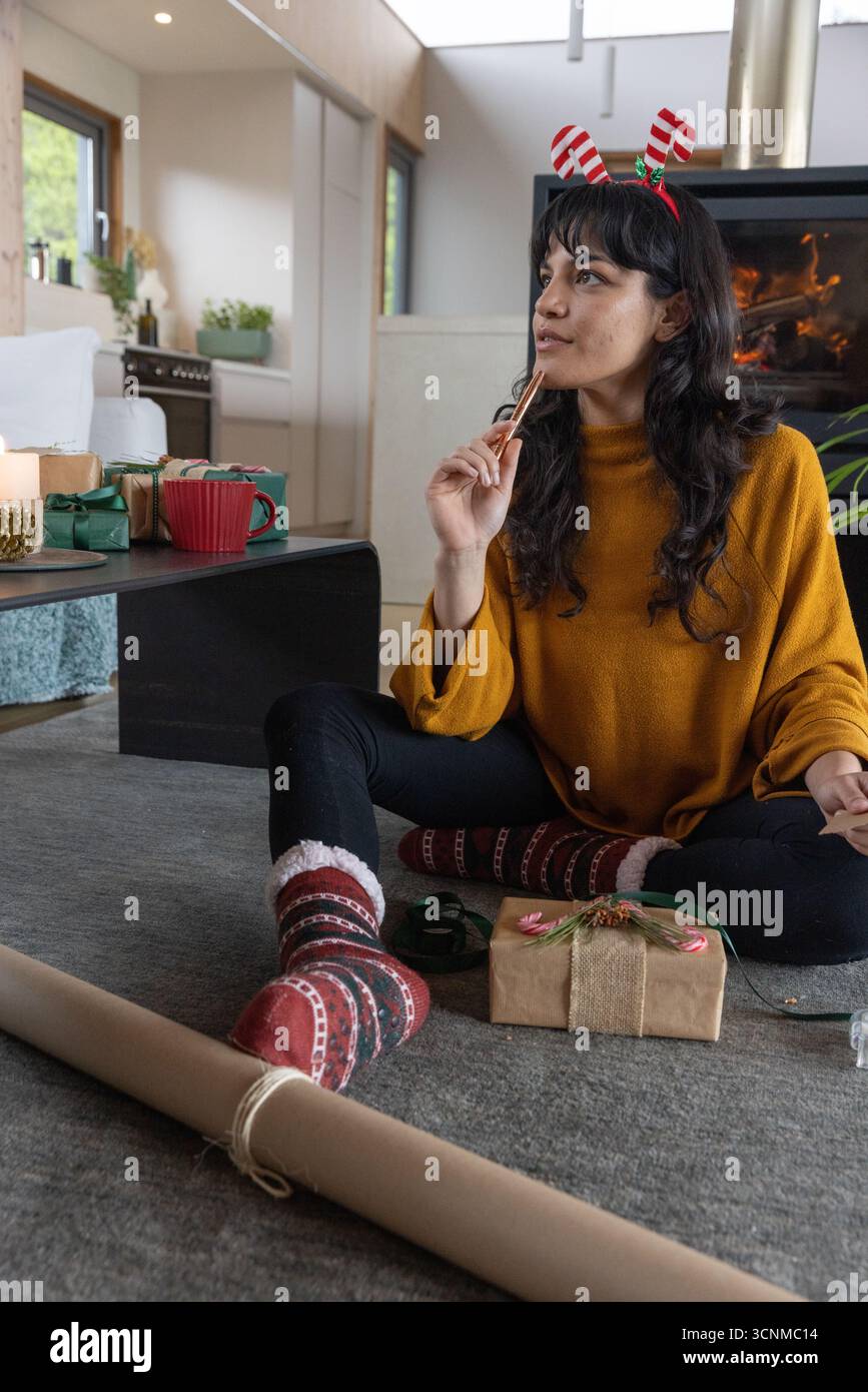 Donna asiatica seduta in casa che tiene il bastone di cannella fissando che avvolge i regali con carta kraft Foto Stock