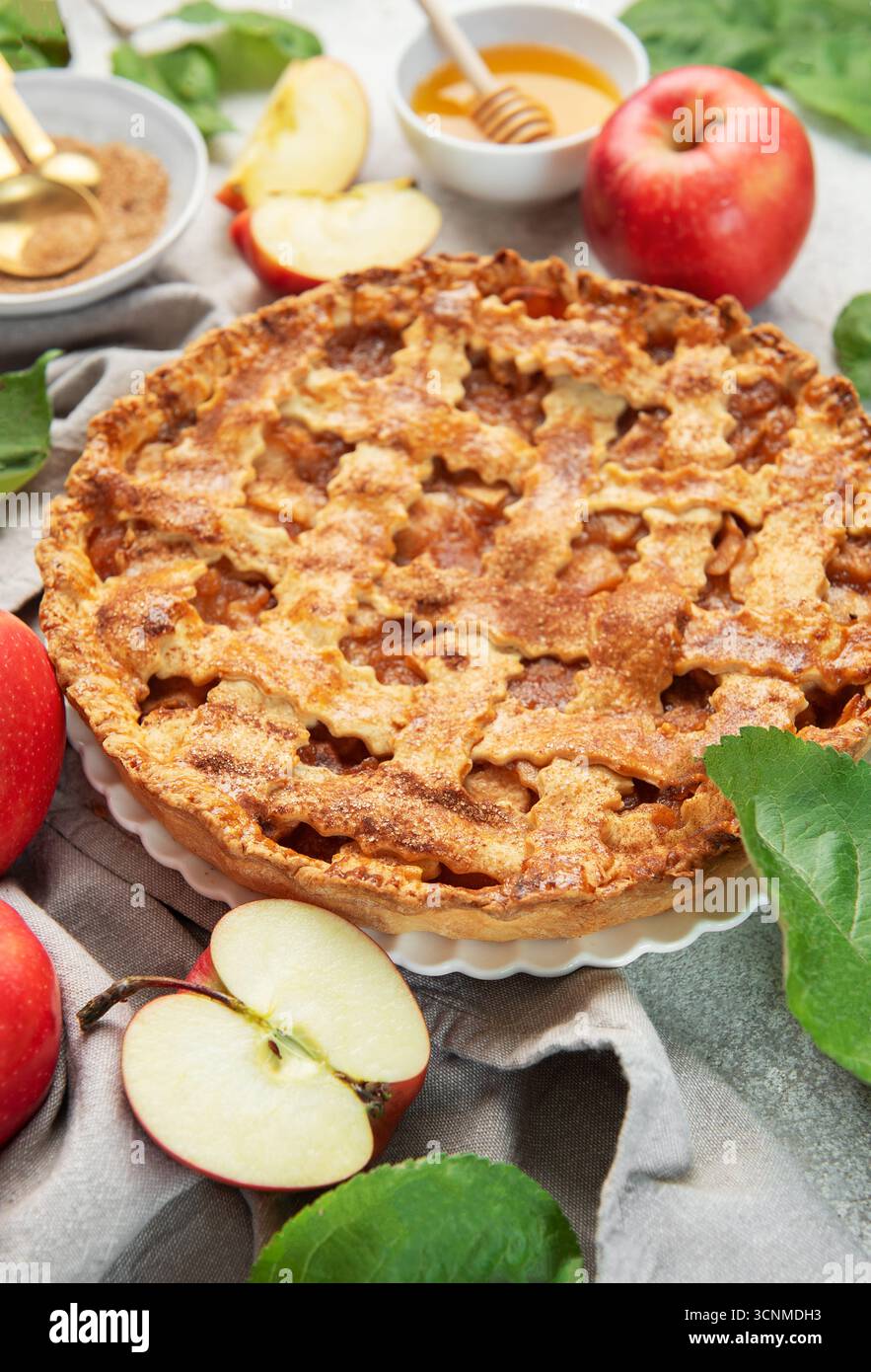 Classica torta di mele circondata da mele fresche, miele, zucchero di canna e decorata con foglie di mele Foto Stock