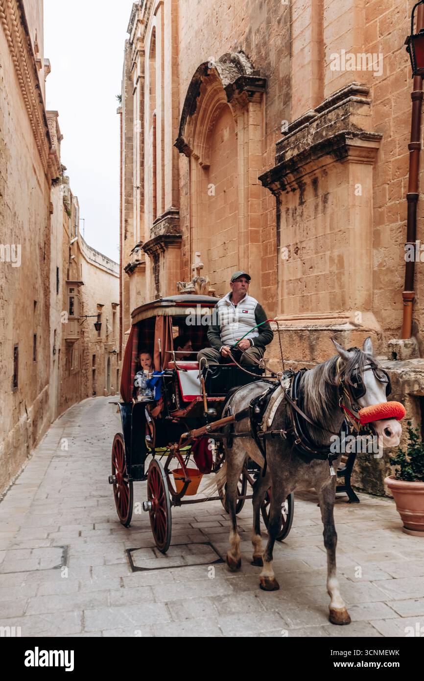 Mdina, Malta - 14 aprile 2025: Tradizionale carrozza trainata da cavalli che trasporta i turisti attraverso le strette e storiche strade di Mdina, con pietra calcarea dorata Foto Stock