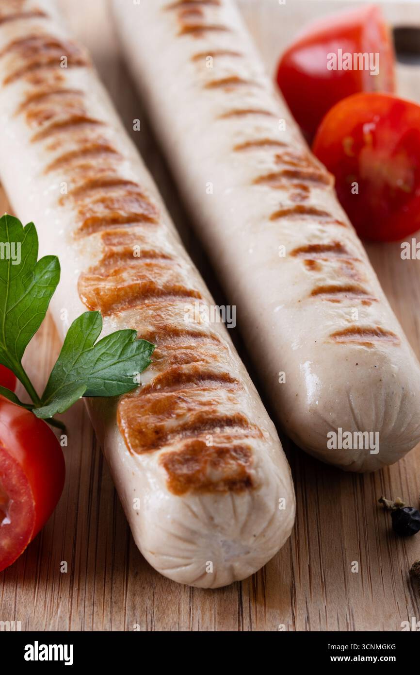 Salsicce Bratwurst grigliate con pomodori ciliegini e prezzemolo isolati su sfondo bianco Foto Stock