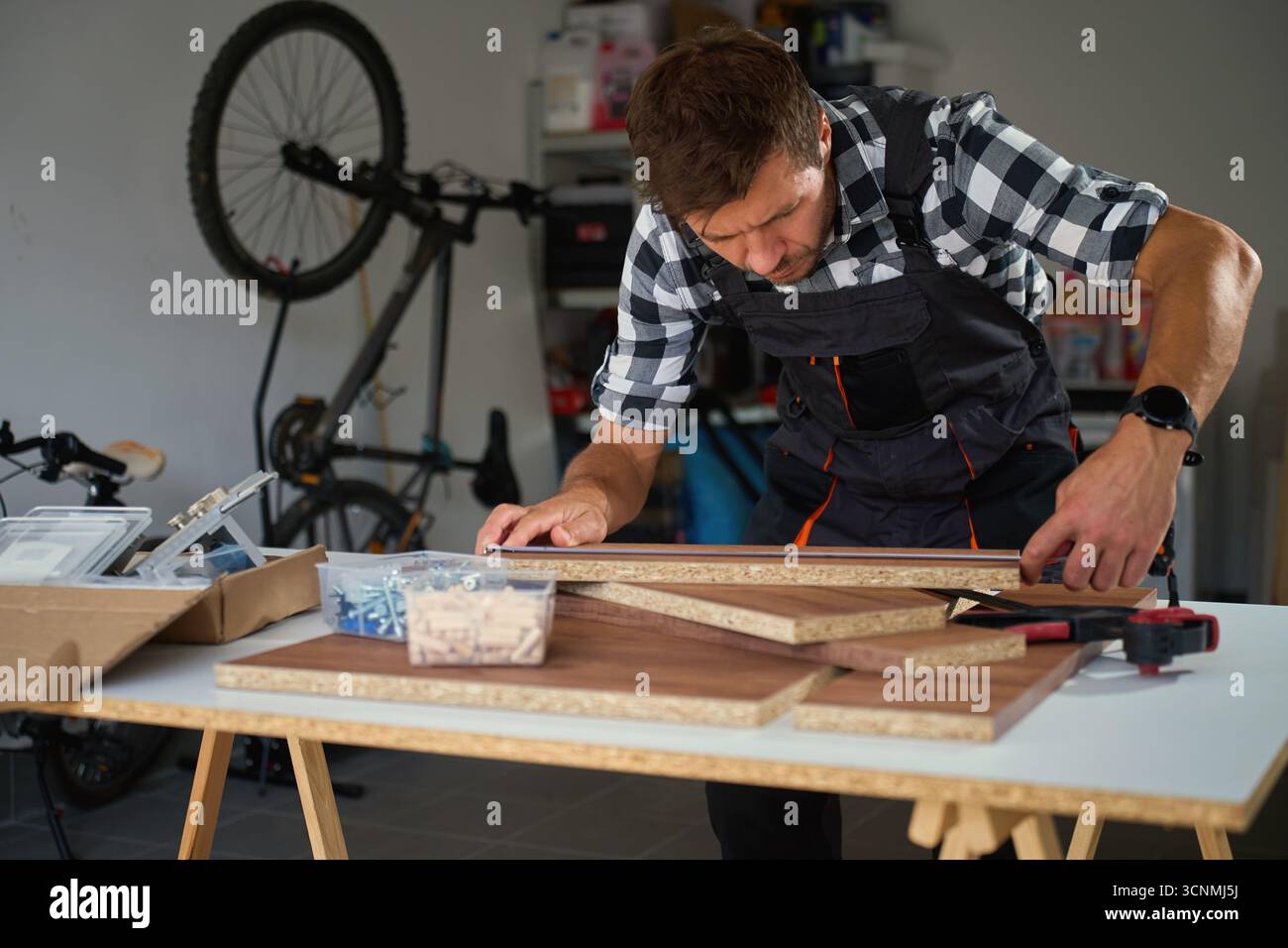 Falegname che misura pannelli in legno in officina con metro a nastro durante l'assemblaggio di mobili. Concetto di lavorazione del legno, produzione di mobili e fai da te Foto Stock
