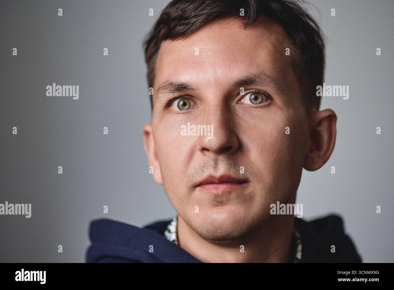 Uomo con capelli scuri corti e occhi verdi in posa in interni Foto Stock