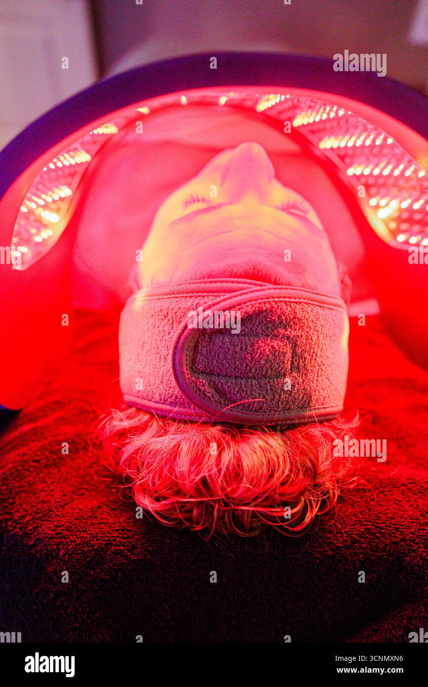 Donna sdraiata che riceve una terapia a luce rossa per ringiovanimento della pelle Foto Stock