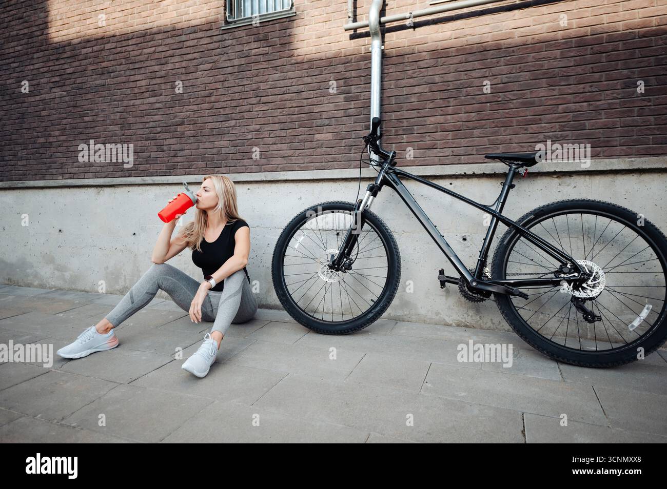 Donna sportiva che beve acqua dopo il ciclismo all'aperto Foto Stock