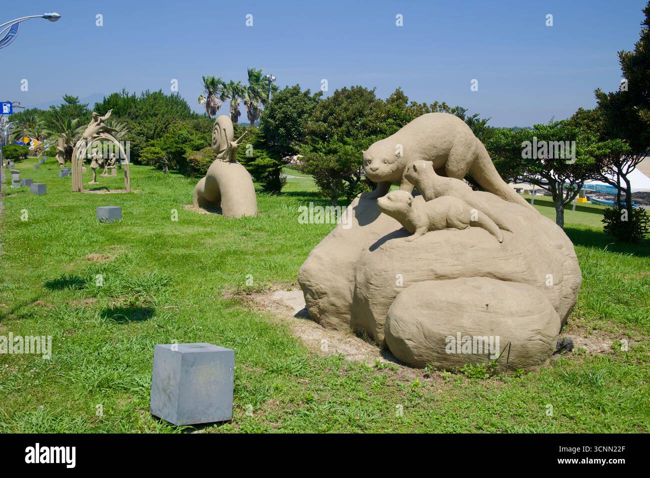 Animali giocosi e sculture di lumaca fiancheggiano il parco erboso accanto alla spiaggia di Pyoseon a Seogwipo, con palme e alberi costieri dietro. L'arte pubblica forma un Foto Stock