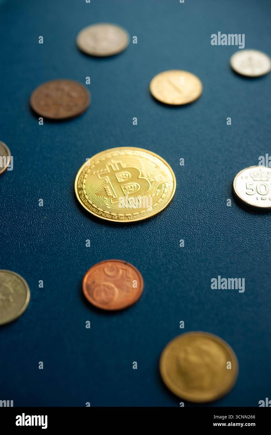 Moneta Bitcoin d'oro tra le monete in valuta tradizionale su sfondo blu evidenziando il contrasto tra denaro digitale e denaro fisico Foto Stock