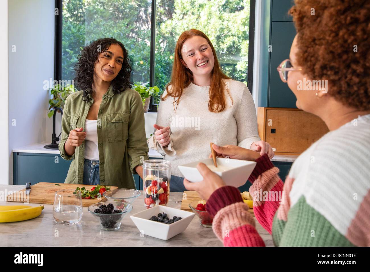 Diverse amiche preparano frutta fresca in cucina con taglieri e utensili Foto Stock
