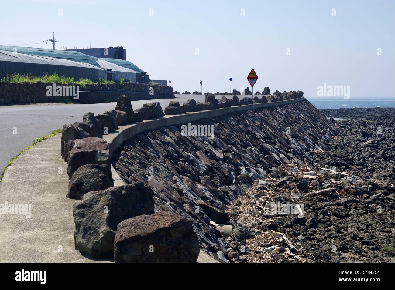 Uno stretto marciapiede segue un'ambizione curva in cemento sopra una riva di roccia lavica vicino a Taeheung, con grandi massi posti come barriera tra la costa Foto Stock