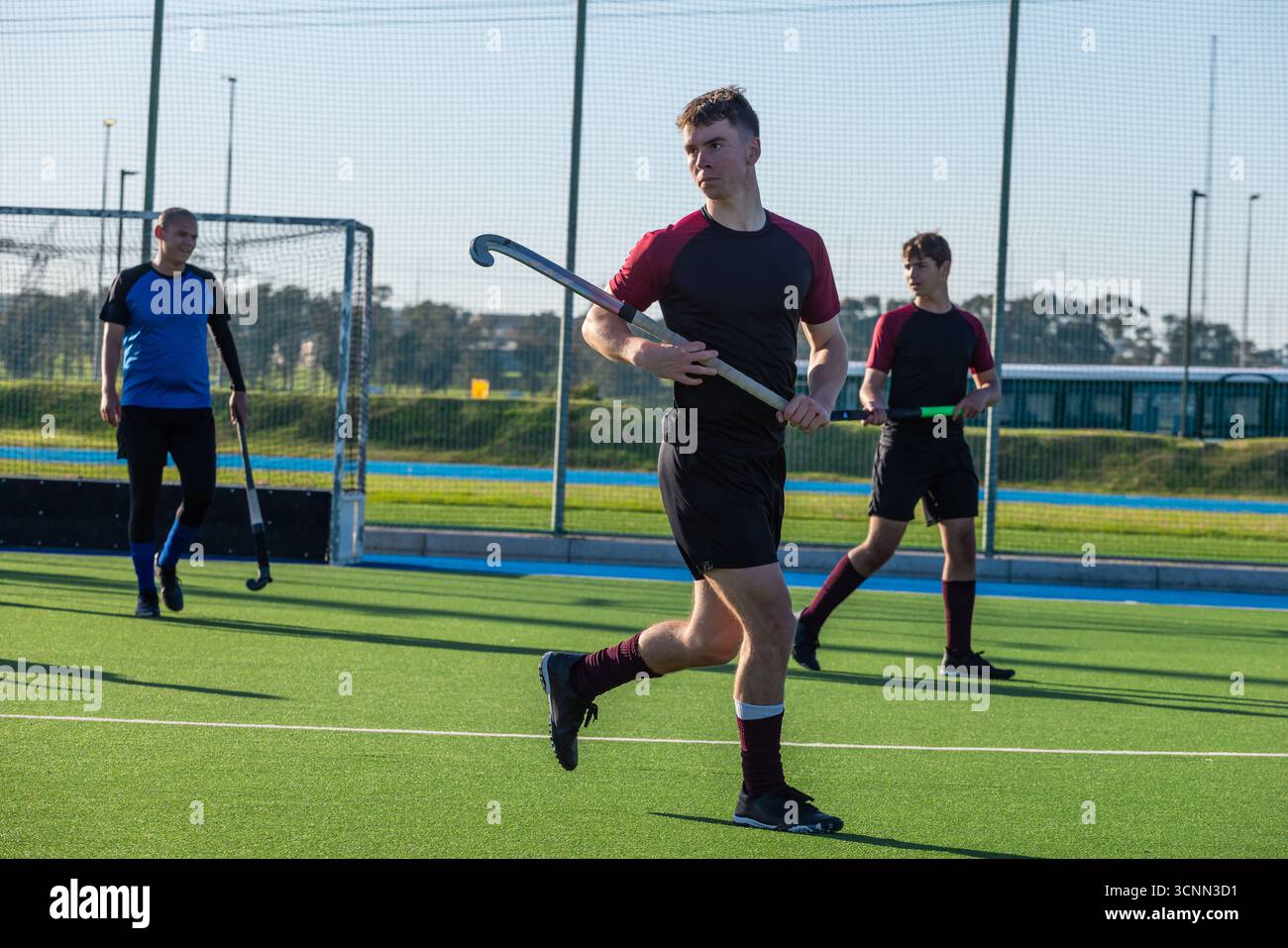 Diversi compagni di squadra maschi che sparano in una gabbia con reti con bastoncini da hockey sul campo da prato Foto Stock