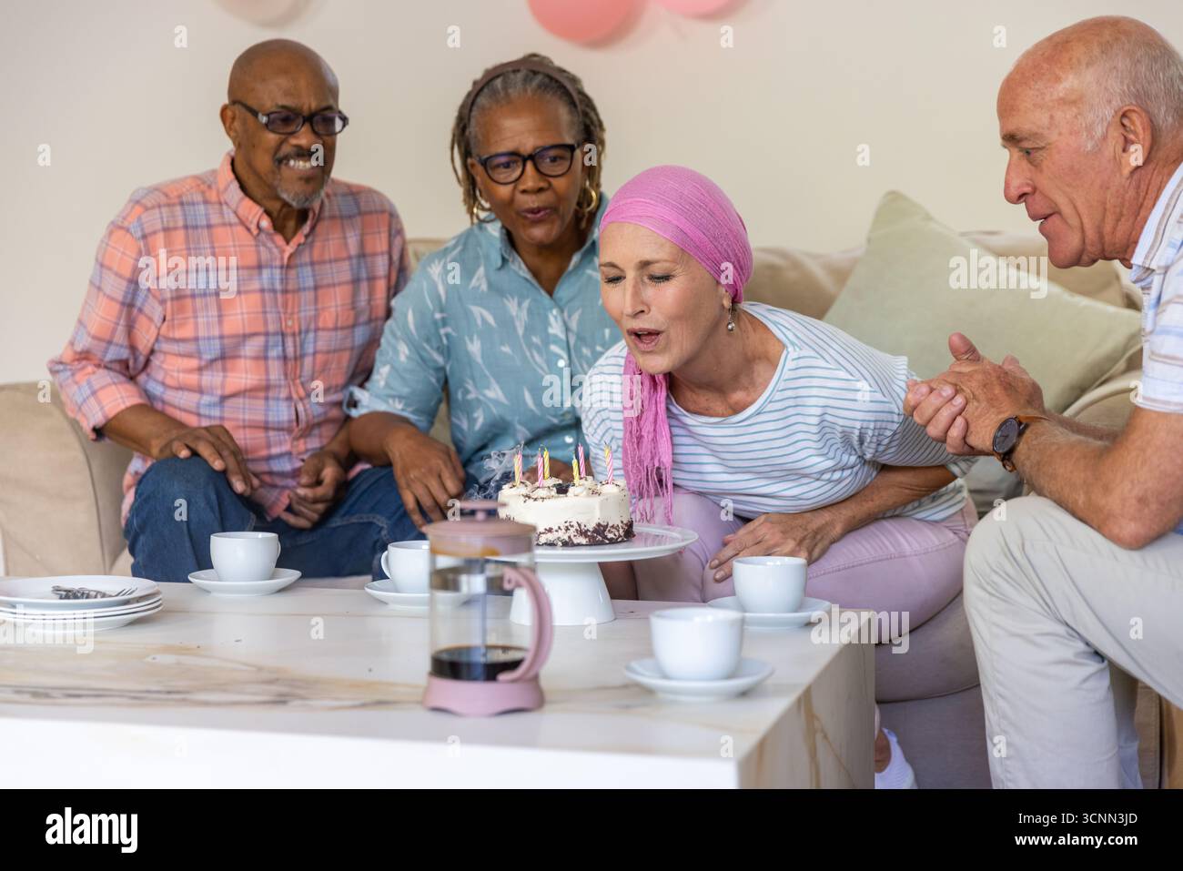 Diversi amici anziani festeggiano il compleanno in salotto con torta, tazze da caffè, stampa francese Foto Stock