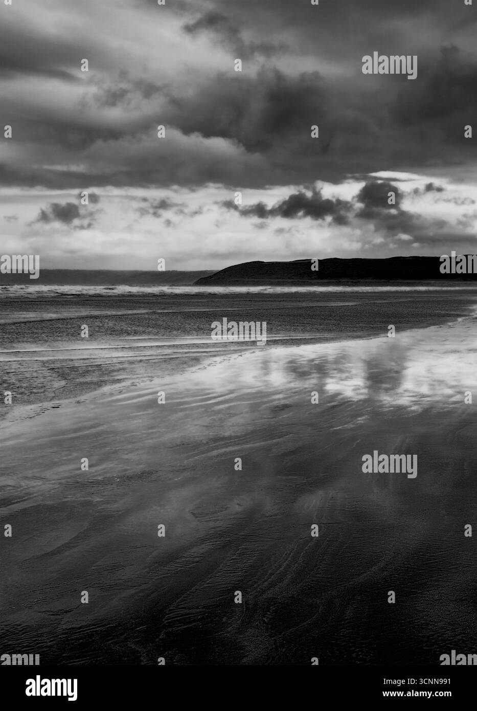 Immagine in bianco e nero di una spiaggia sabbiosa illuminata dalla luna di notte, nuvole sopra un promontorio lontano, adatto per una copertina del libro Foto Stock