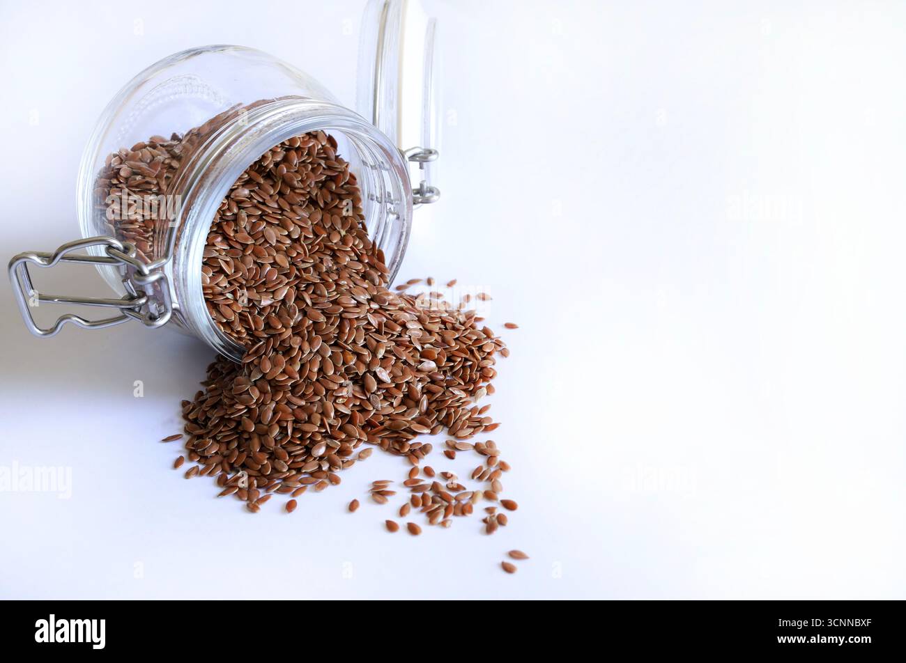 Semi di lino versati da un vaso di vetro isolato su sfondo bianco. I semi di lino sono ricchi di fibre, acidi grassi omega-3 e lignani. Foto Stock