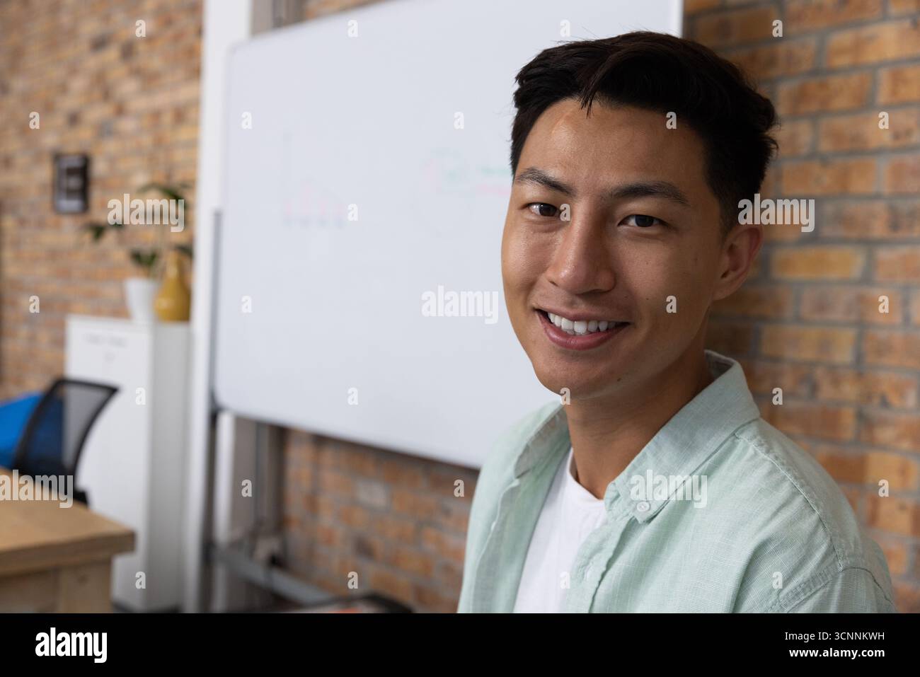 Uomo asiatico sorridente nell'area riunioni con lavagna mobile, impianto, spazio di copia Foto Stock