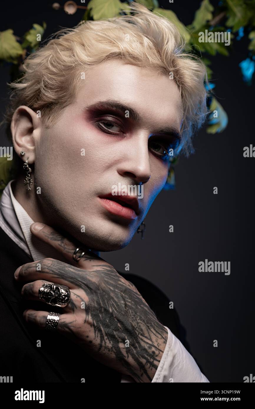 Un giovane e affascinante uomo presenta il suo epico costume di Halloween con un trucco spettacolare e accessori audaci. Foto Stock