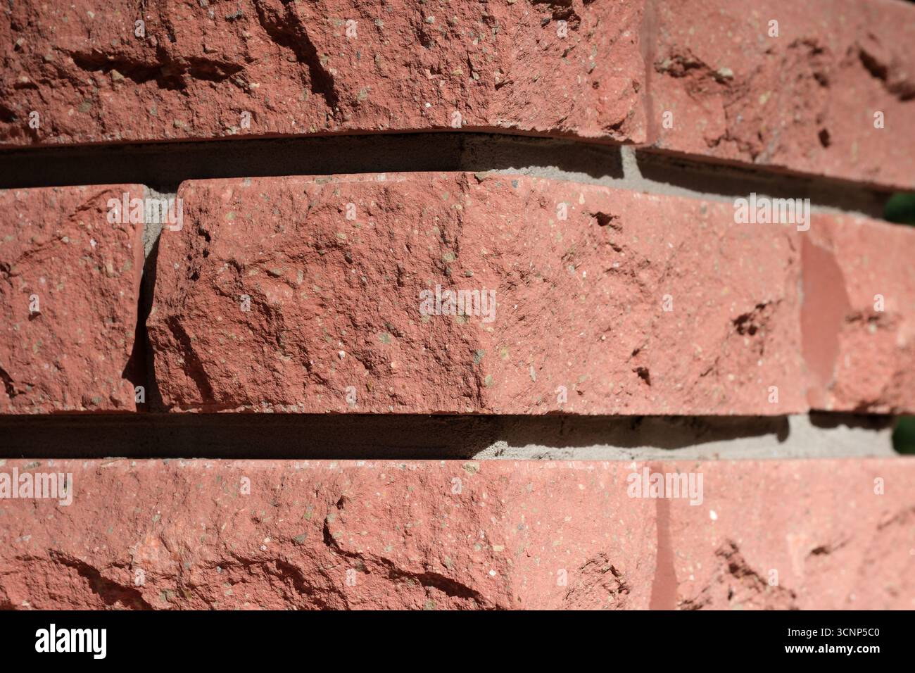 La calda luce del sole mette in risalto la consistenza ruvida delle pareti in mattoni rossi a mezzogiorno. Foto Stock