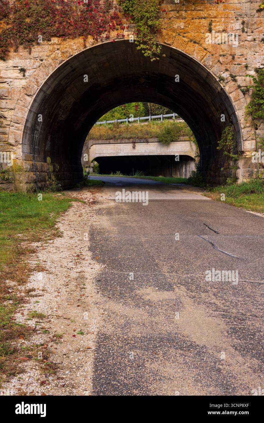 Una strada che passa sotto un vecchio ponte ad arco in pietra. Foto Stock