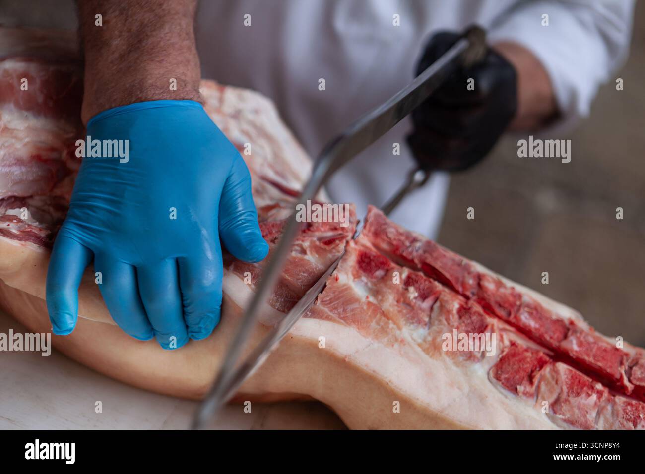 Macellaio segando mezzo maiale sul suo blocco Foto Stock