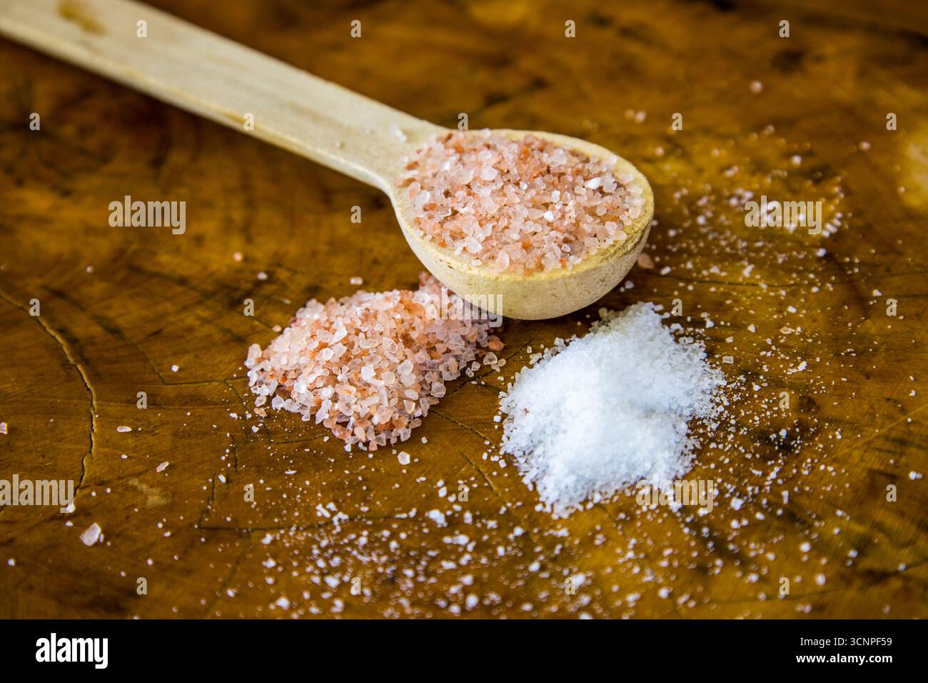 Un cucchiaino di legno di sale rosa dell'Himalaya con un piccolo mucchio di sale bianco da tavola e sale rosa dell'Himalaya Foto Stock