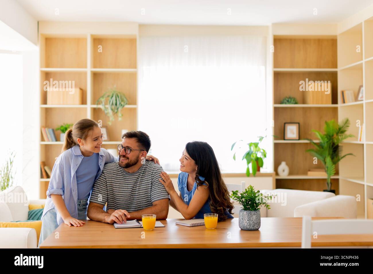 Una famiglia allegra condivide momenti di gioia in una stanza illuminata dal sole, coinvolgendo in vivaci conversazioni e risate durante la colazione e le attività. Foto Stock