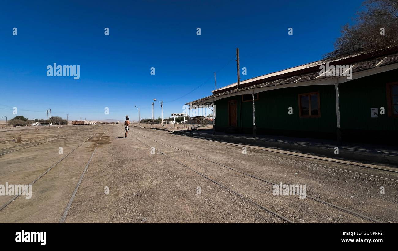Uomo che tiene il figlio sulle spalle e cammina sopra la vecchia stazione ferroviaria di Baquedano in Cile. Nel deserto di Atacama si trova il museo del villaggio. Foto Stock