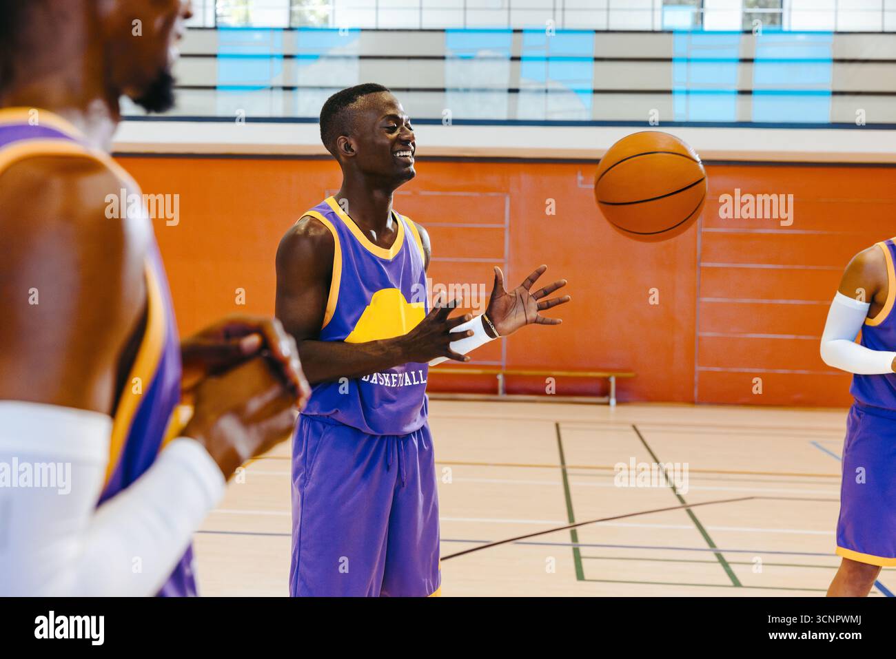 Giovani giocatori di basket che si divertono in una sessione di allenamento al chiuso, indossando uniformi di squadra, trasmettendo lavoro di squadra, emozioni e azione in campo con un tocco di vivacità Foto Stock